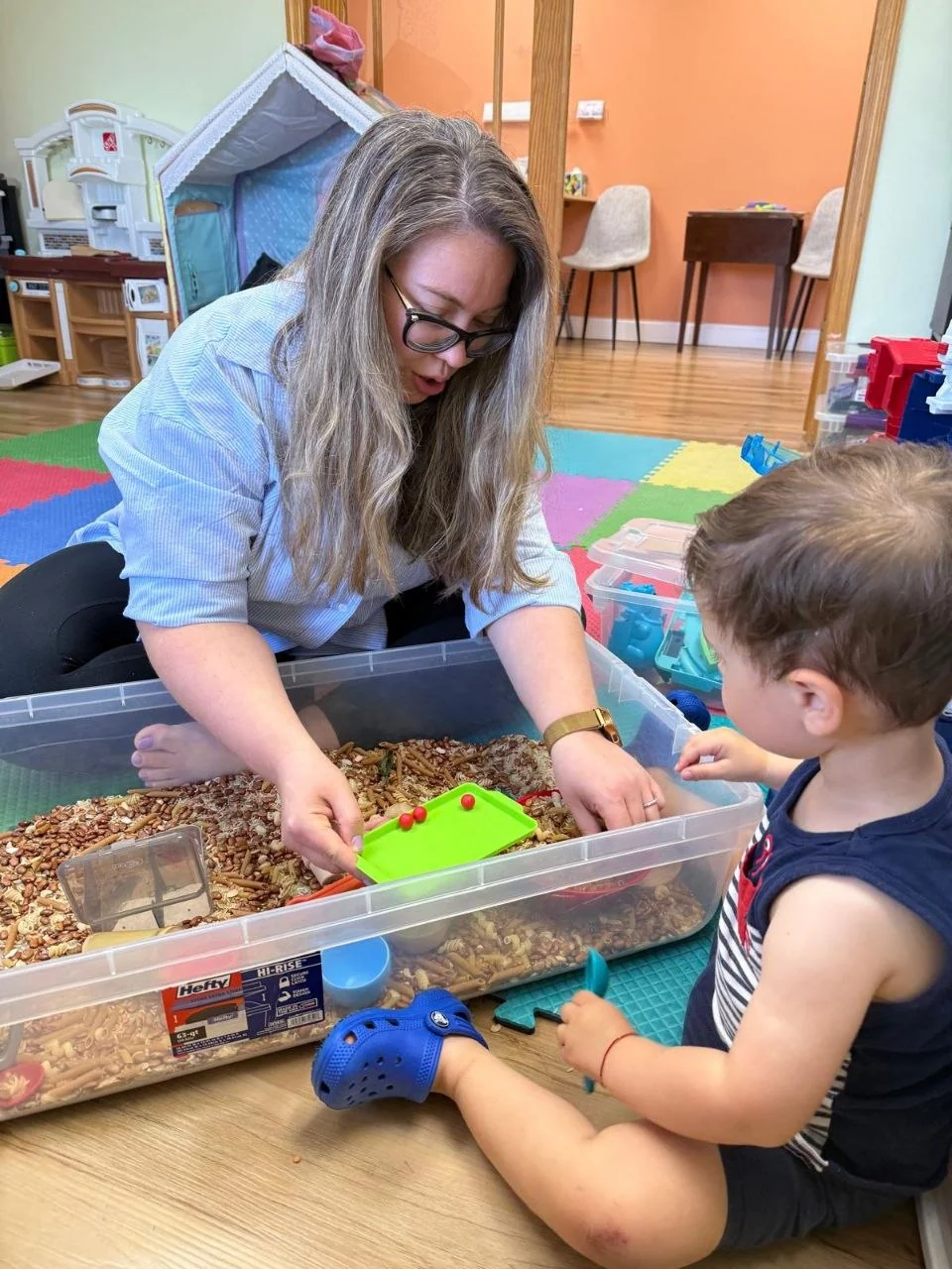 Speech-language pathologist using play-based therapy with a child in a sensory bin.